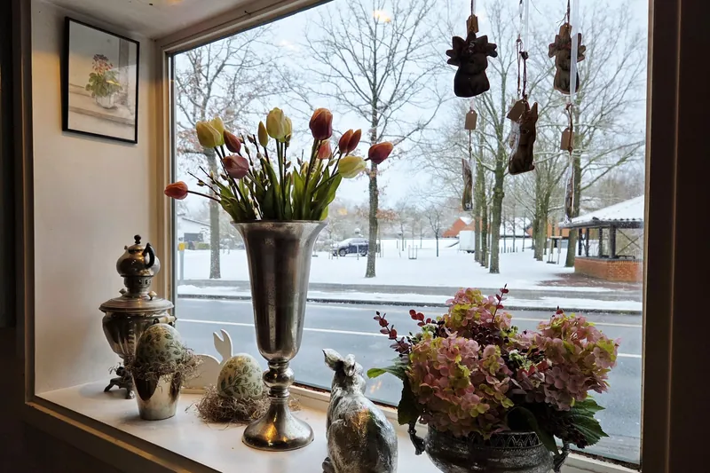 Fensterbank mit Tulpen, Samowar und Osterdekoration, draußen verschneite Bäume