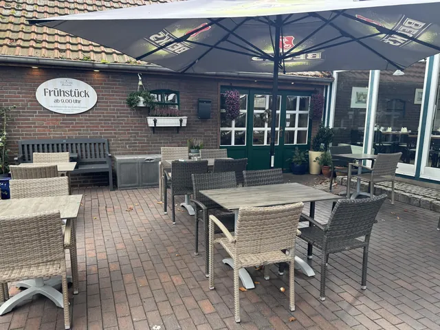 Terrasse mit Korbstühlen und Sonnenschirm vor der Backsteinfassade, daneben der Wintergarten