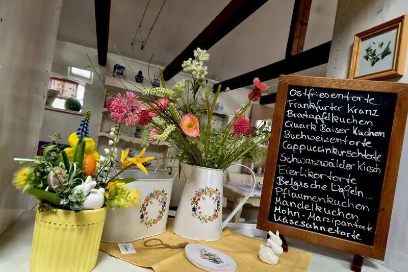 Handgeschriebene Tafel mit den Torten des Tages, daneben Frühlingsblumen